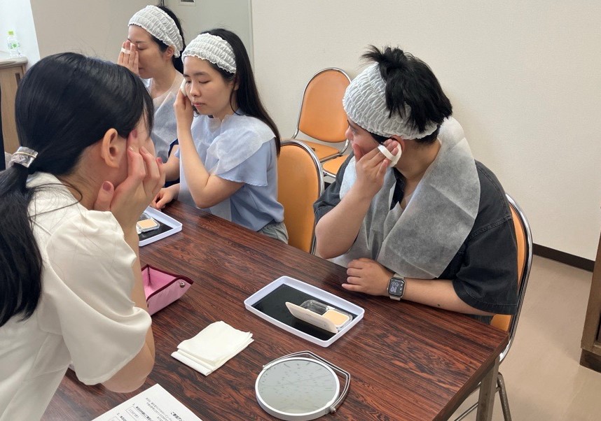 大阪府立大阪南視覚支援学校でおこなったときの様子を写した写真。生徒さんは対面でファンデーションのつけかたをレクチャーしてもらっています