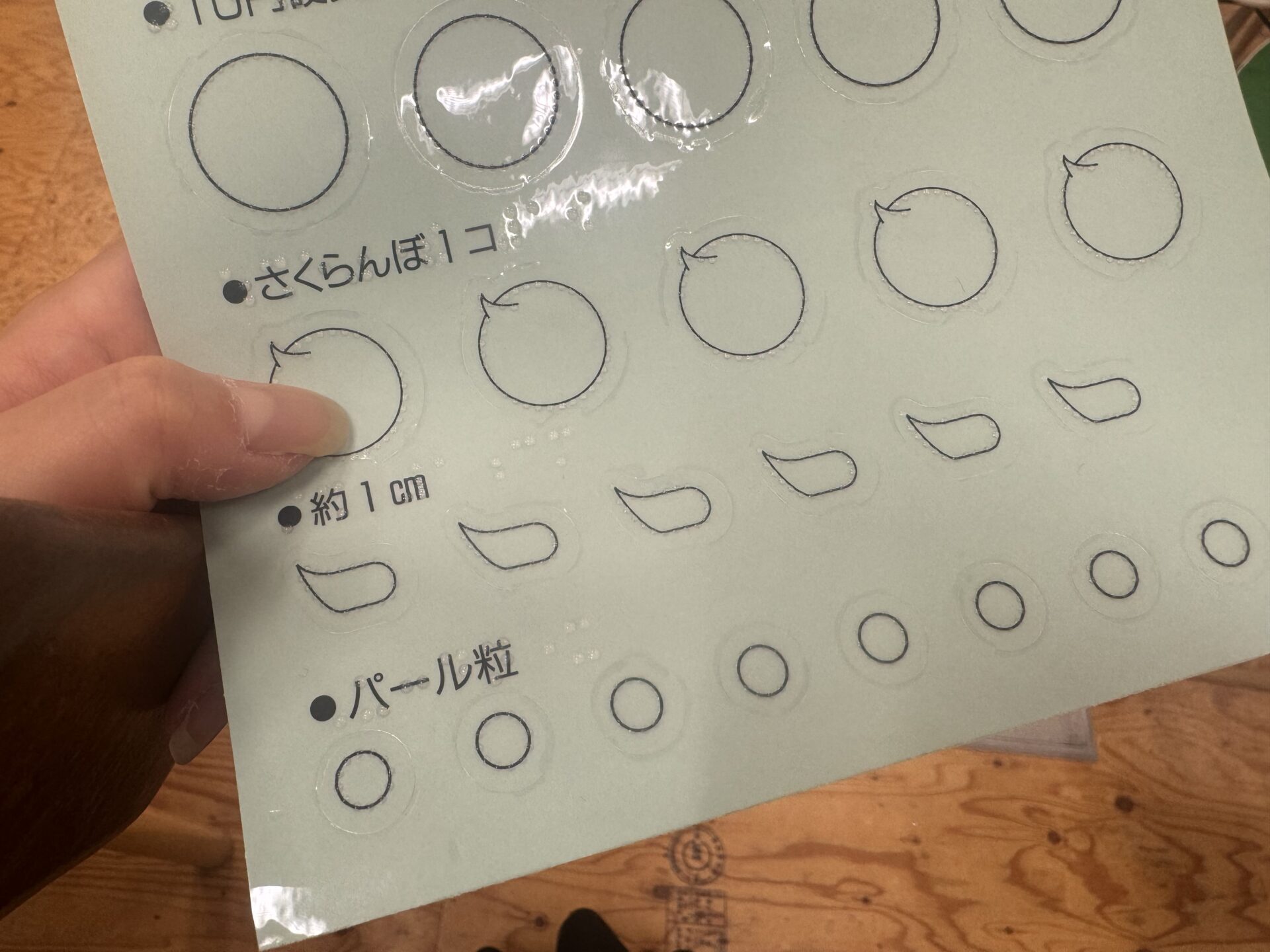 点字シールの写真。透明なシールにとつてんがついており、さくらんぼいっこ、約1センチ、パール粒など、コスメでよくでてくるワードがさわってわかるようになっています