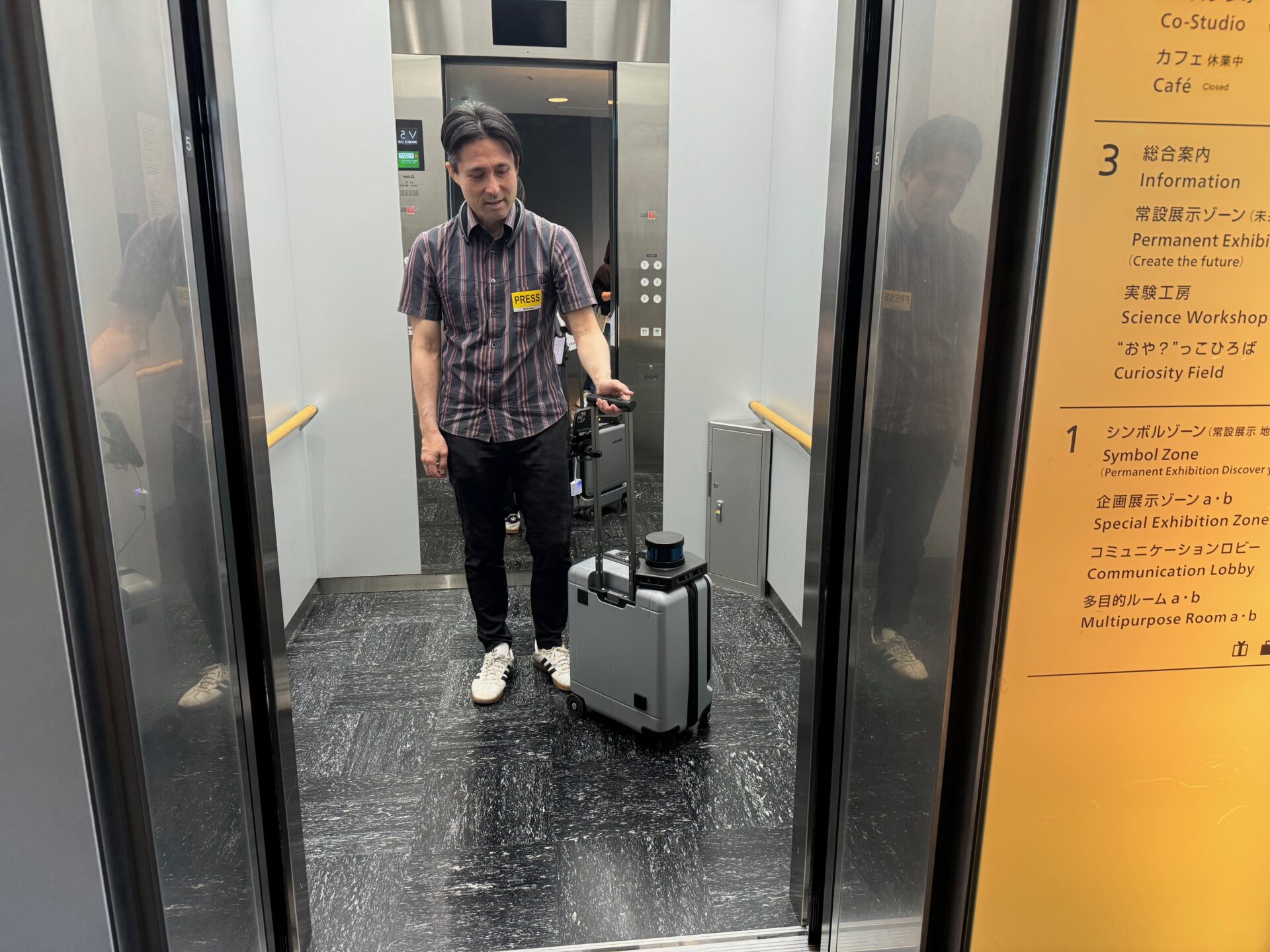 エレベーターの外から、エレベーターのなかにいるしらとりさんを写した写真。エーアイスーツケースとともにエレベーターの中央あたりにしらとりさんがいます